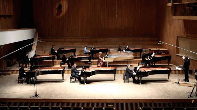 ステージ右端に立つ指揮者に向かうように配置されたグランドピアノと演奏たちを客席から写した写真