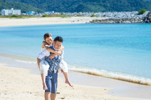 沖縄の海辺を新婦をおんぶしている新郎